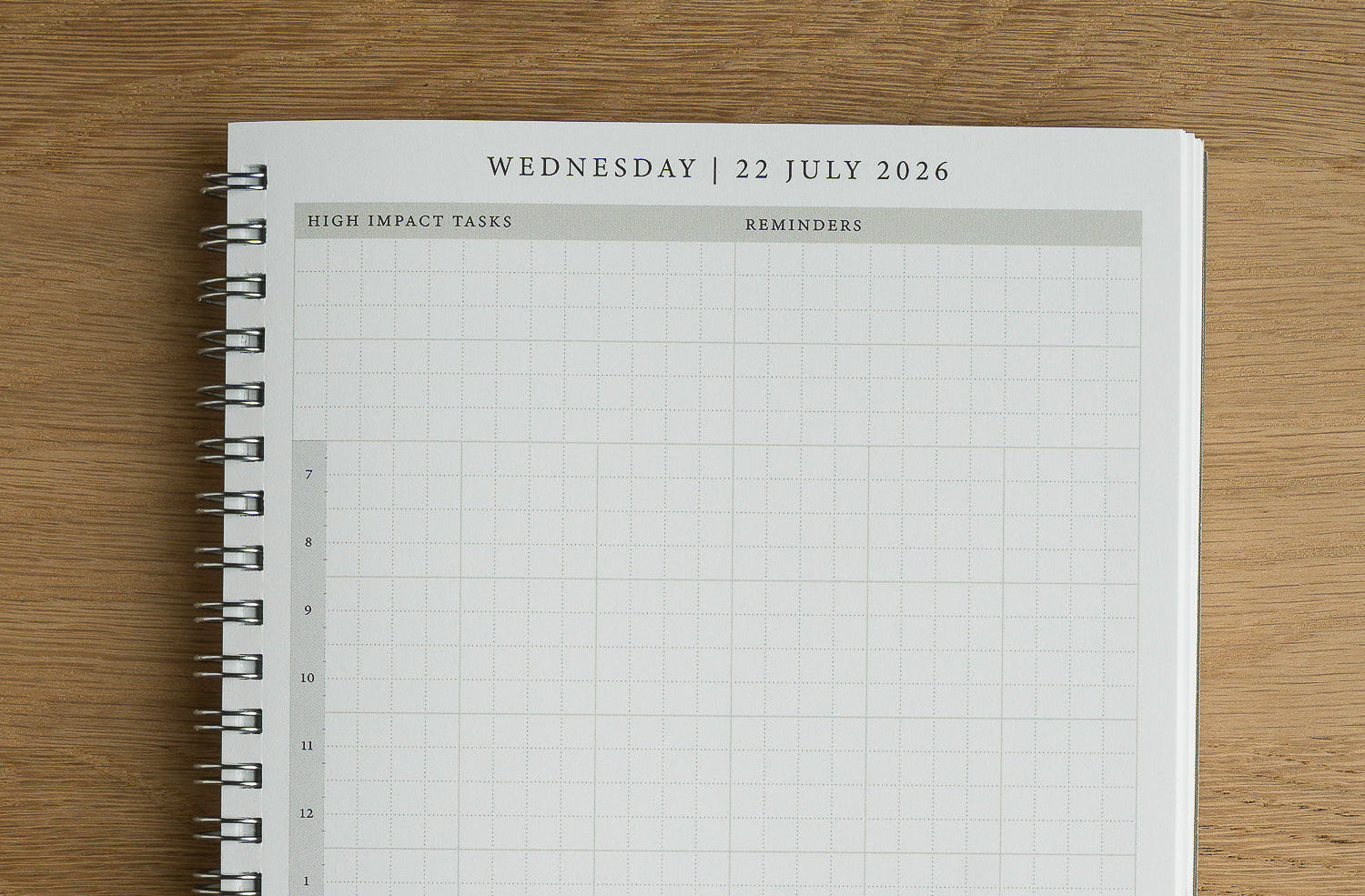 A spiral-bound planner page from a weekly grid planner, showing Wednesday, 22 July 2026, with columns for high impact tasks and reminders, placed on a wooden surface.